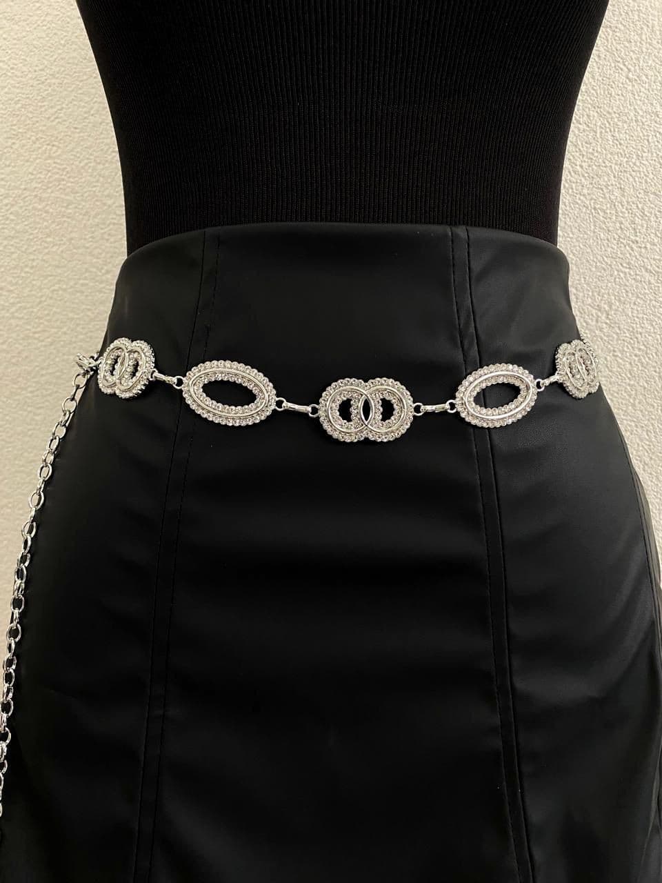 Cinto corrente de argolas duplas e cravejadas com strass, em dourado e prateado, usado sobre saia preta de couro sintético.