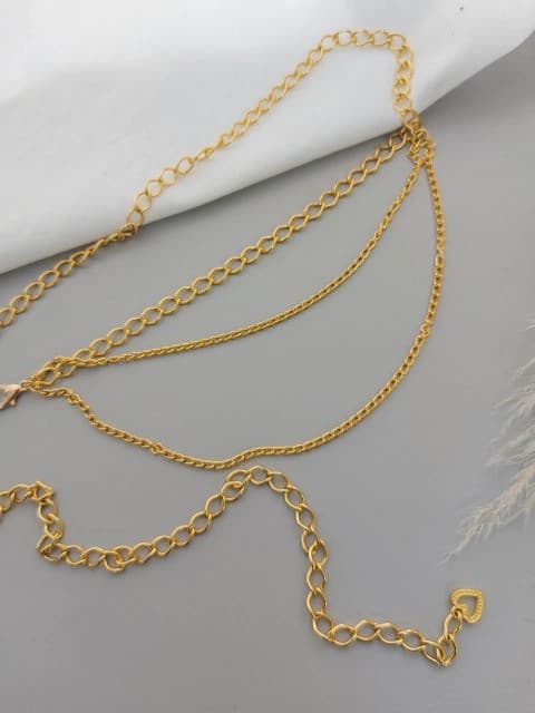Cinto de corrente dourada com três voltas de elos de diferentes espessuras e alongamento, sobre um fundo cinza e branco.