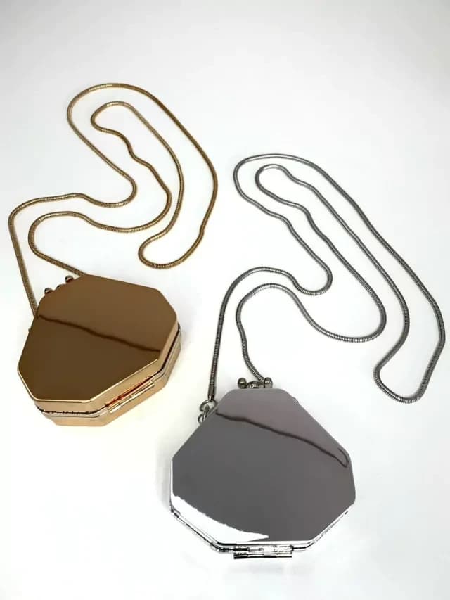 Mini bolsas clutch de festa hexagonais, espelhadas: uma dourada e uma prateada, com alças de corrente fina, em fundo branco.