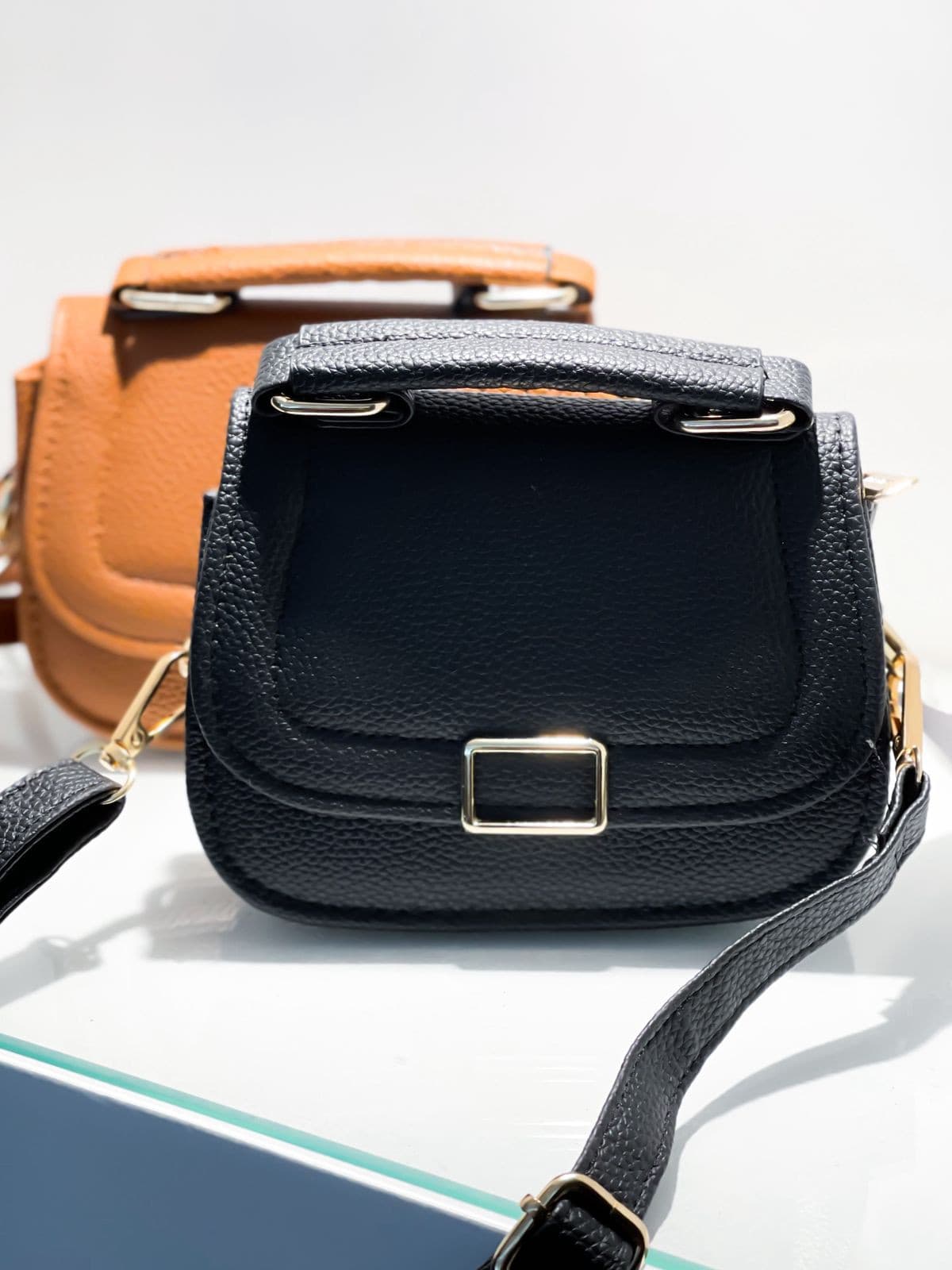 Bolsas mini femininas com textura e alça de mão, sendo uma preta em primeiro plano e outra marrom (caramelo) desfocada ao fun