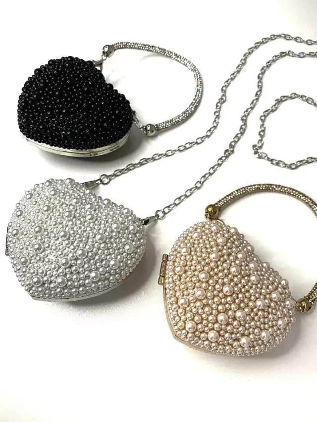 Mini bags em formato de coração com pérolas e strass nas cores preta, branca e bege, ideais para looks femininos elegantes.